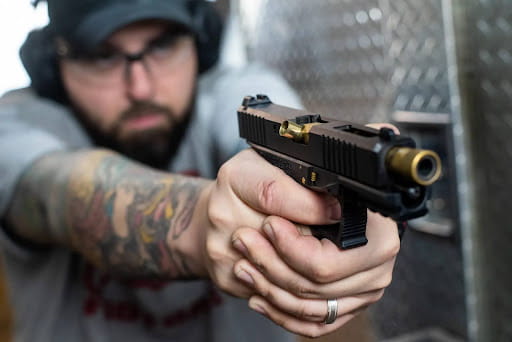 Focus Is On The Gun As A Man Is Shooting It. He Is Blurred Out In The Background With Both Eyes Open As He Shoots.